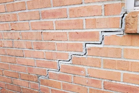 Close-up view of a brick wall with a prominent zigzag crack indicating foundational damage, before repair by MDH Foundation Repair.